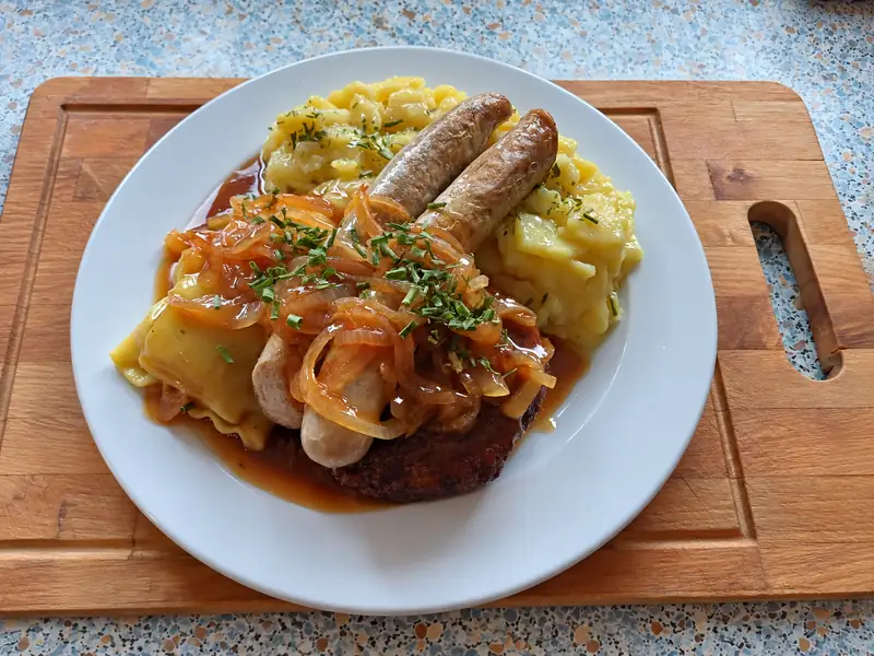 Unser Gartenstüble-Teller mit Maultasche, Bratwurst, Fleischküchle, Kartoffelsalat und Zwiebelsoße